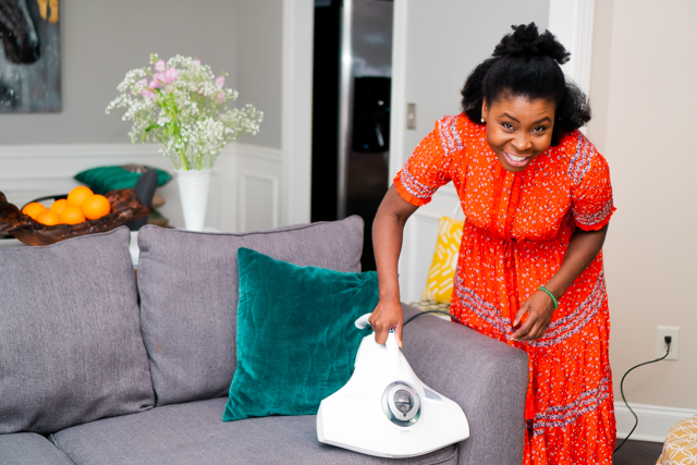 Woman in an orange dress smiling and vacuuming a pillow