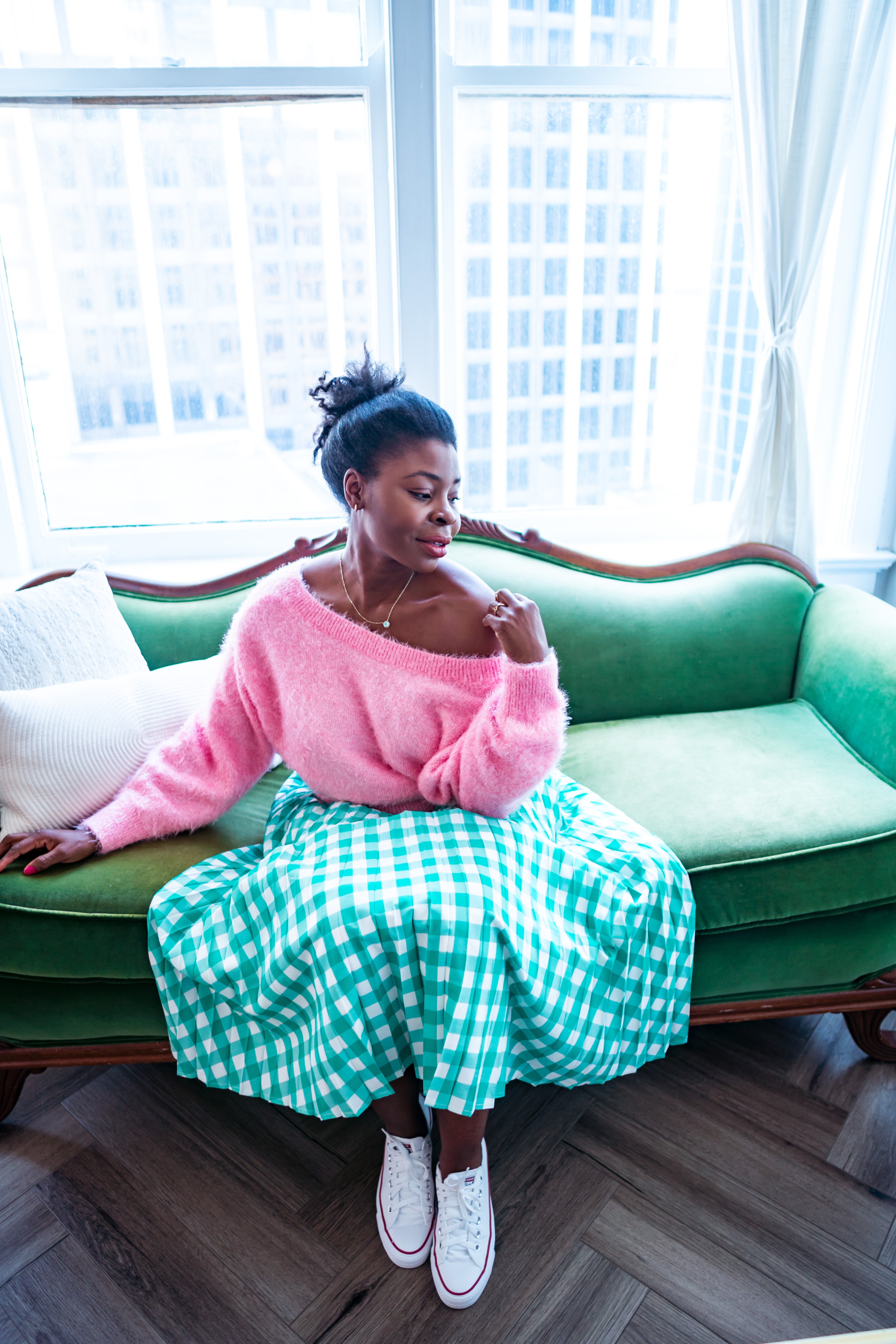 Woman sitting on a green sofa near a large window touching her shoulder